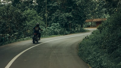 穿黑夹克的人白天骑摩托车上路